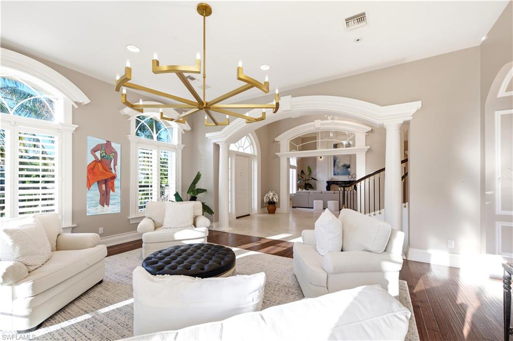 High ceilings, arched windows with plantation shutters, wood-finish flooring, and an ornate chandelier