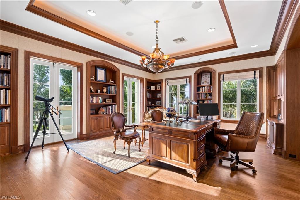 Hardwood flooring, tray ceiling with recessed lighting, integrated wooden shelving, double French doors, and a chandelier