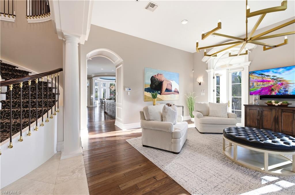 Open-concept living space featuring hardwood flooring, a brass geometric chandelier, and abundant natural light from multiple glass doors and windows