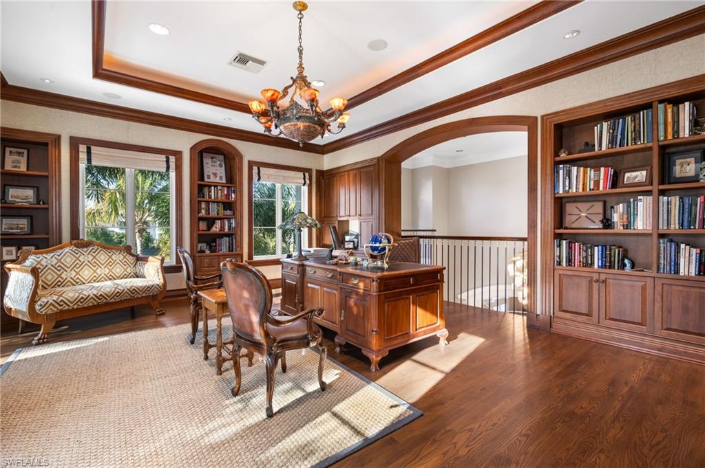 Hardwood flooring, coffered ceiling, built-in shelving, arched doorway, and a decorative chandelier