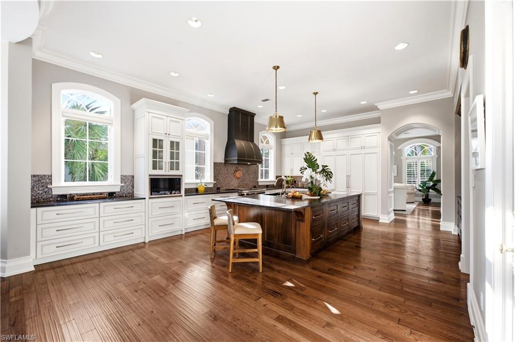 Hardwood flooring throughout, a large central island with integrated storage, white perimeter cabinetry, recessed lighting, and arched windows