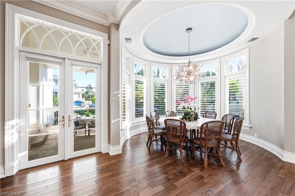 Wood-finish flooring, French doors with transom, curved wall with plantation shutters, coffered ceiling with recessed lighting, and a chandelier