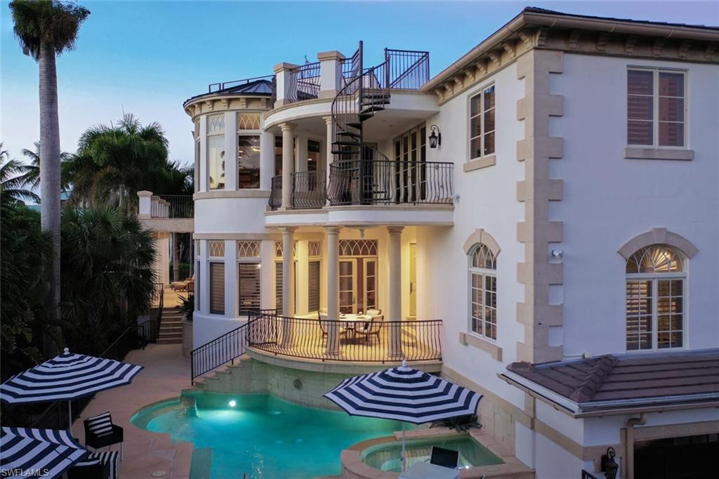 Exterior featuring a swimming pool, integrated spa, multiple balconies with wrought iron railings, a spiral staircase, and exterior columns