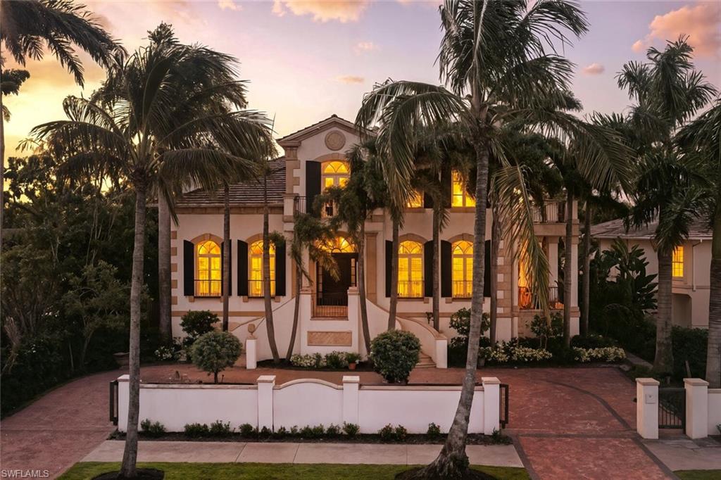 Stucco exterior with a tiled roof, arched windows, decorative shutters, and mature palm trees