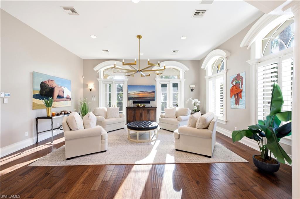 Spacious interior featuring wood-finish flooring, high ceilings, multiple arched windows with plantation shutters, and a modern chandelier