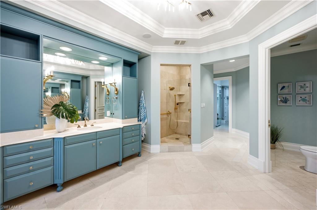 Spacious bathroom featuring a built-in vanity with dual sinks, a large mirror, a glass-enclosed shower, and crown molding
