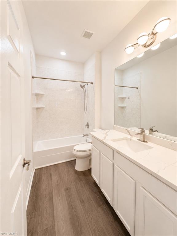 Bathroom featuring wood-finish flooring, a white vanity with an integrated sink and light-toned countertop, a tile-surround tub/shower combination, and a modern light fixture