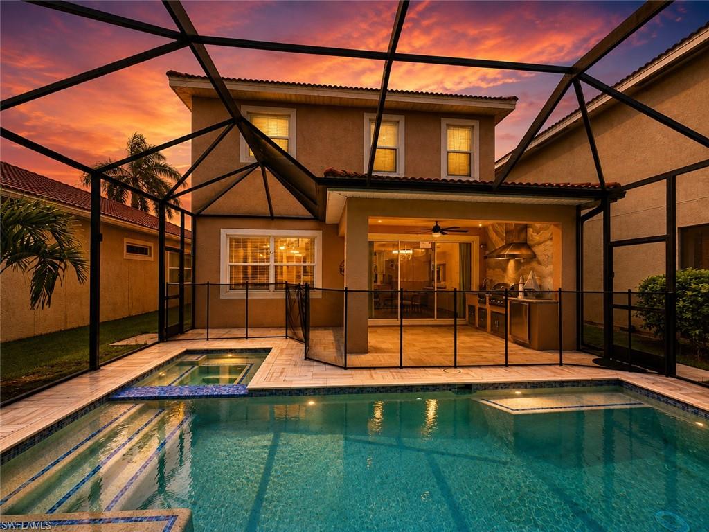 Screened outdoor living area featuring a swimming pool, integrated spa, and an outdoor kitchen with built-in appliances