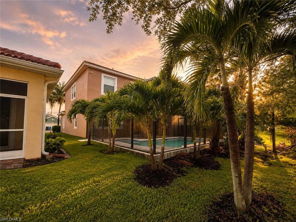 Expansive lawn with mature palm trees, screened pool enclosure, and exterior stucco finish