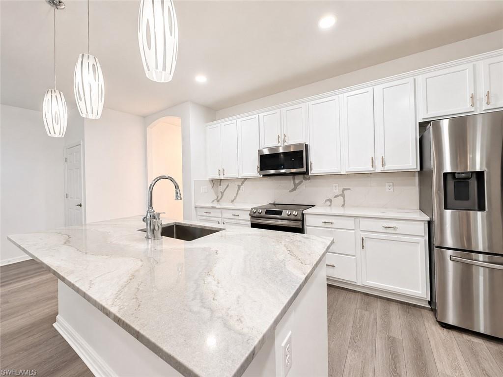 Kitchen island with a stainless steel sink and gooseneck faucet, white shaker cabinets, stainless steel appliances, and light wood-finish flooring