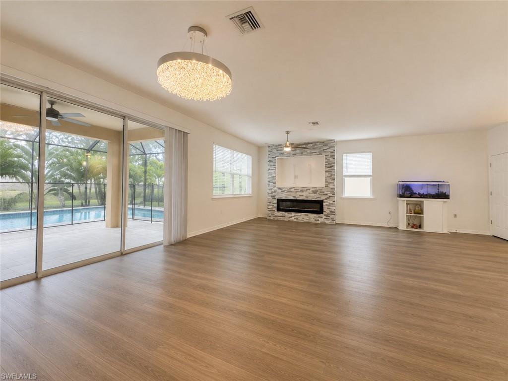Expansive living area featuring wood-finish flooring, a contemporary chandelier, and a fireplace with a stacked stone facade