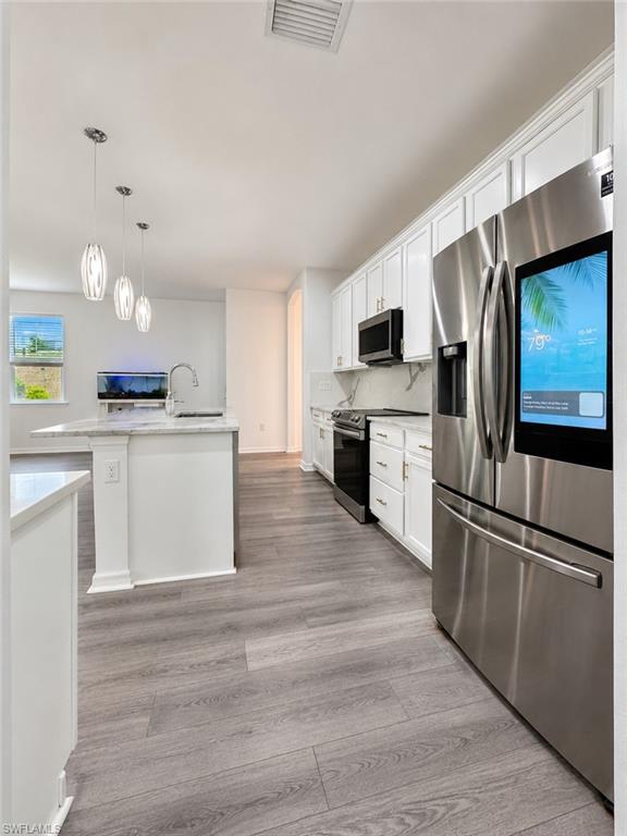 Kitchen featuring a center island, stainless steel appliances, white cabinetry, and wood-finish flooring