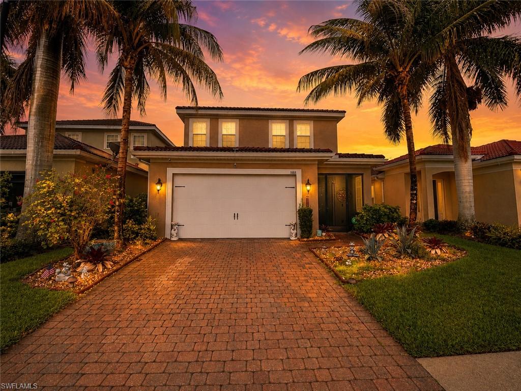Brick paver driveway, lush landscaping, two-story stucco exterior, integrated garage, and a covered entry
