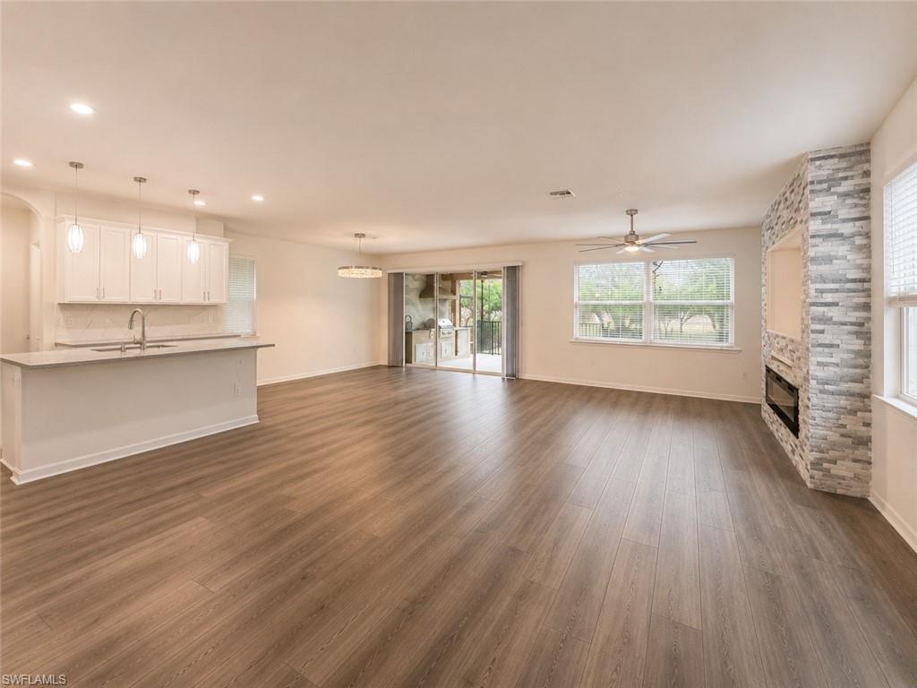 Open-concept living space featuring wood-finish flooring, a kitchen island with pendant lighting, a stone-clad fireplace with an integrated media niche, and sliding glass doors to the exterior