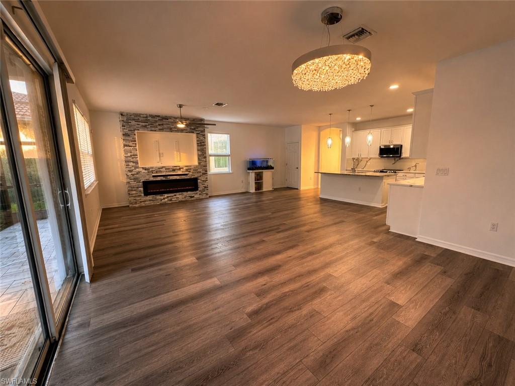 Open-concept living area with wood-finish flooring, a stacked stone accent wall with an electric fireplace, sliding glass doors, a modern chandelier, and a breakfast bar