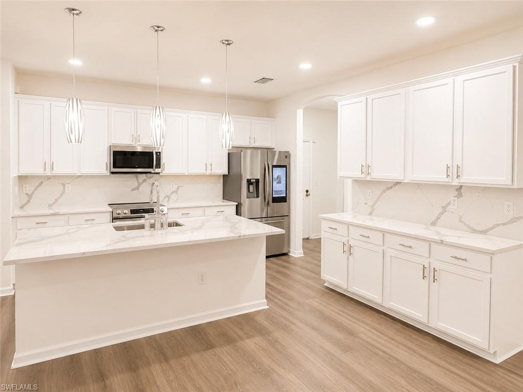 Kitchen featuring white shaker cabinetry, an island with countertop seating, stainless steel appliances, pendant lighting, and wood-finish flooring