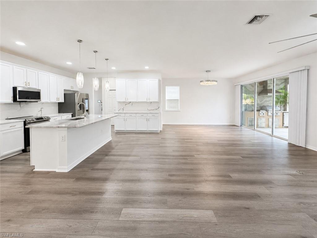 Open concept living area featuring wood-finish flooring, a kitchen island with stone countertop, white shaker cabinetry, stainless steel appliances, and sliding glass doors