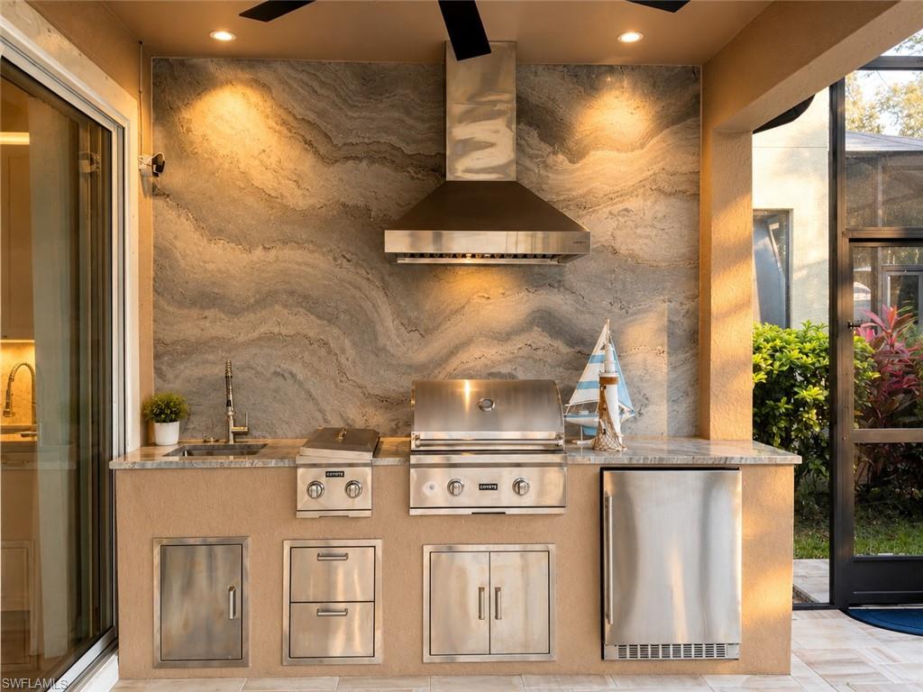 Outdoor kitchen featuring a stone backsplash, stainless steel appliances, built-in grill, sink, and undercounter refrigeration