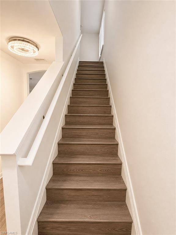 Wood-finish staircase with white risers and railing, featuring a contemporary ceiling light fixture