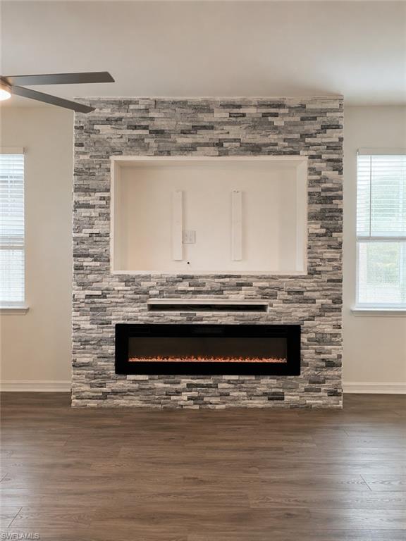 Stacked stone accent wall with integrated linear electric fireplace, wood-finish flooring, and a ceiling fan