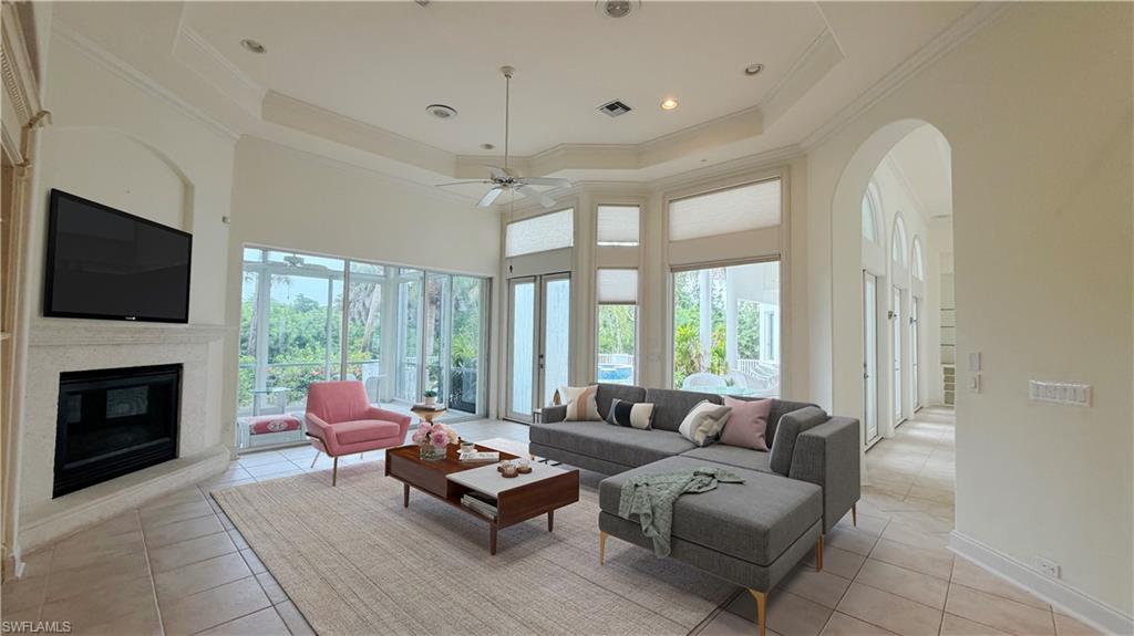 Living area featuring a tray ceiling, recessed lighting, a fireplace with a stone surround, expansive windows, and tiled flooring