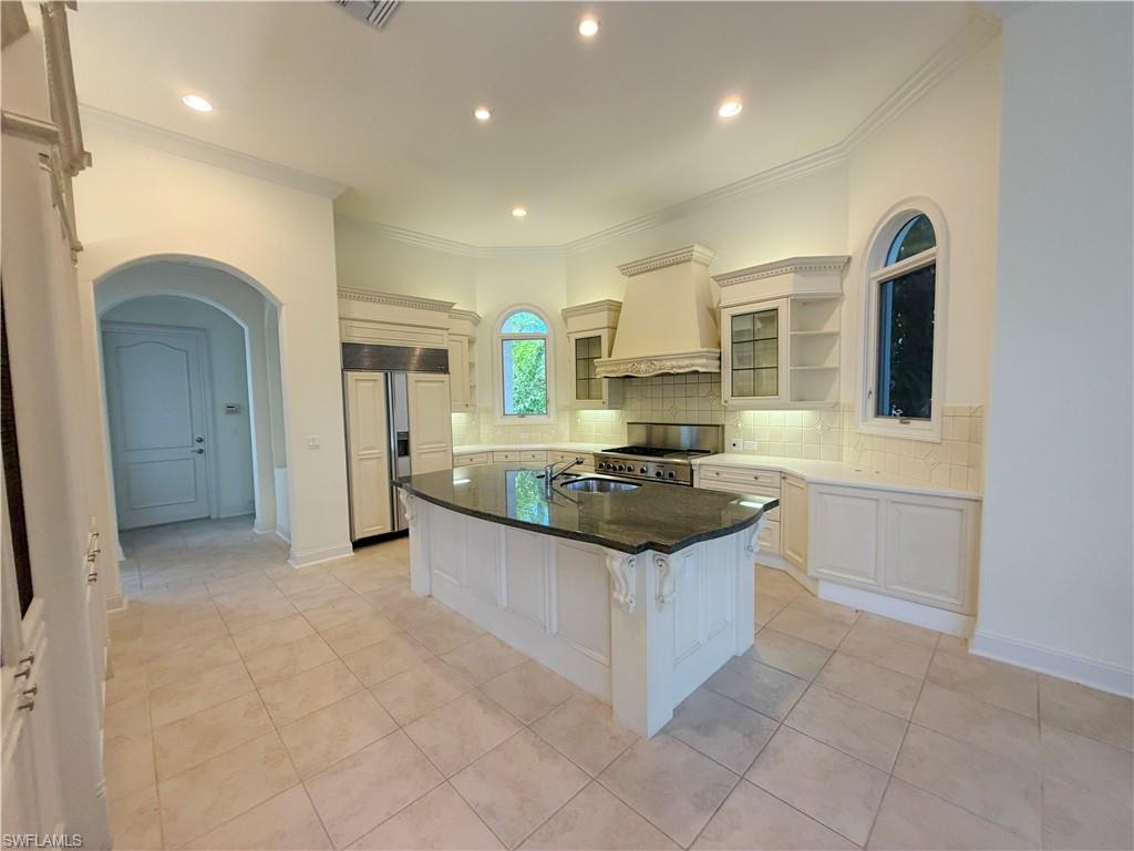 Gourmet kitchen with a large island featuring a double sink, stainless steel appliances, custom cabinetry, tiled flooring, and arched windows