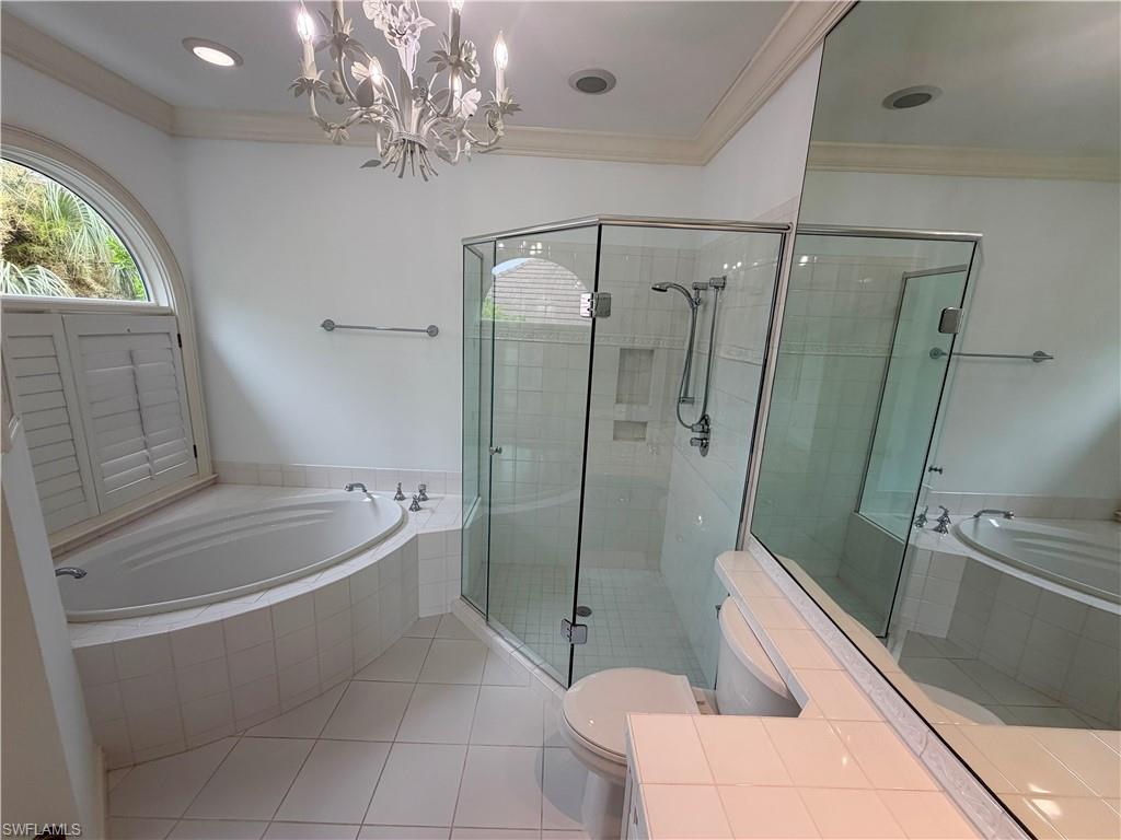 Recessed lighting, tile flooring, glass-enclosed shower, built-in bathtub, and an arched window with plantation shutters