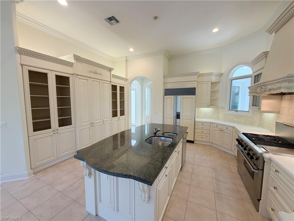 Spacious kitchen featuring an expansive center island with dual sinks, extensive built-in cabinetry, ceramic tile flooring, and a stainless steel range