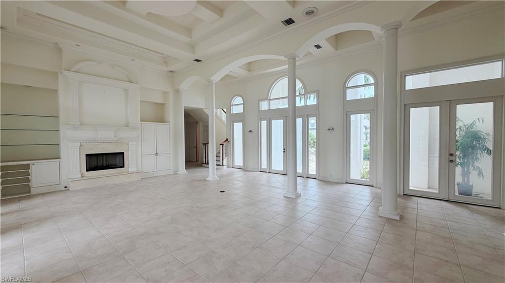 Spacious interior featuring a coffered ceiling, floor-to-ceiling windows, built-in shelving, a fireplace, and column details