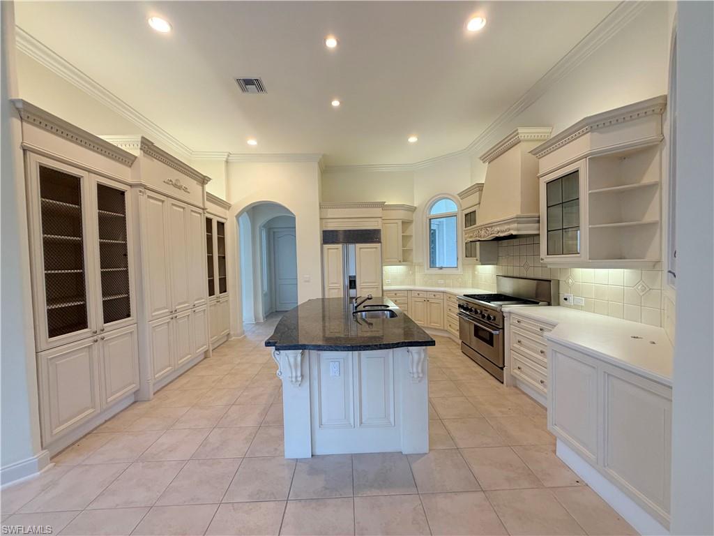 Gourmet kitchen featuring a large central island with dark countertop, extensive cabinetry with glass and solid fronts, stainless steel range, and tile flooring