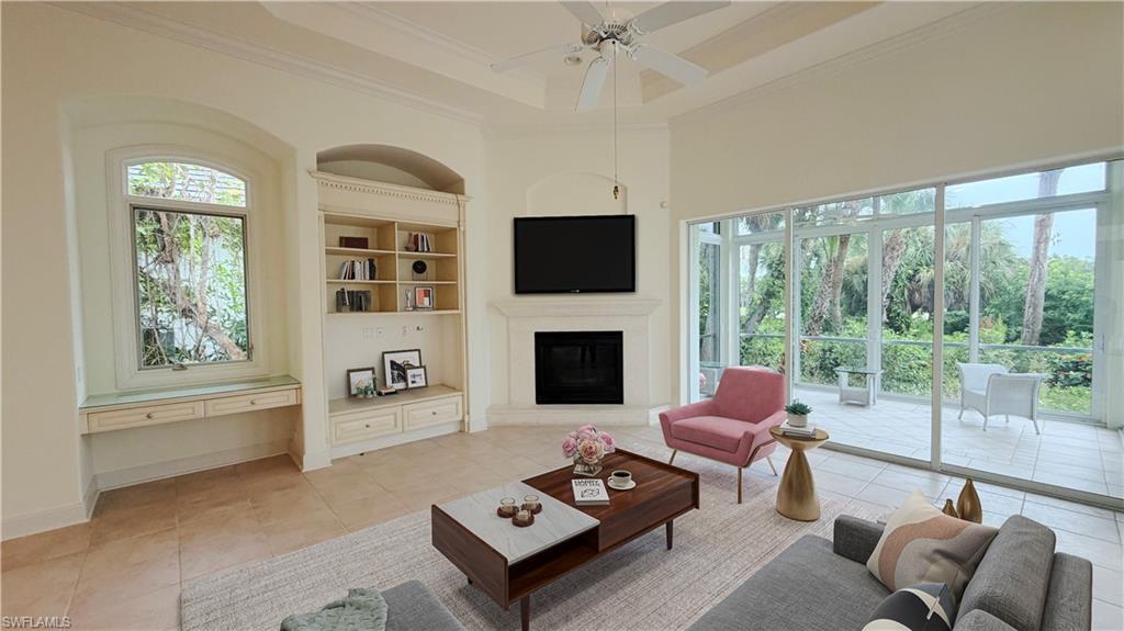 Spacious room with coffered ceiling, built-in shelving, corner fireplace, and expansive sliding glass doors leading to a screened outdoor living area