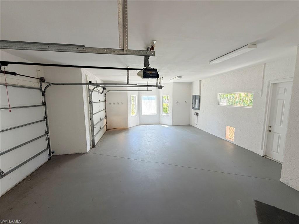 Spacious garage featuring two overhead doors, painted concrete flooring, multiple windows, and a side entry door