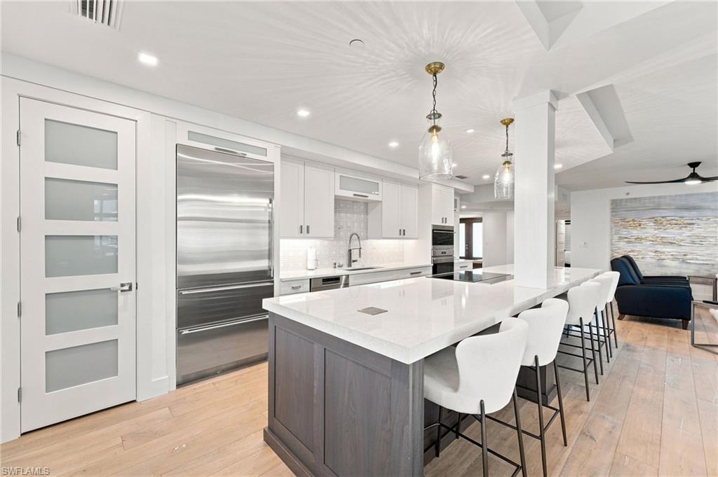Gourmet kitchen featuring a large island, integrated stainless steel refrigerator, recessed lighting, white cabinetry, and wood-finish flooring