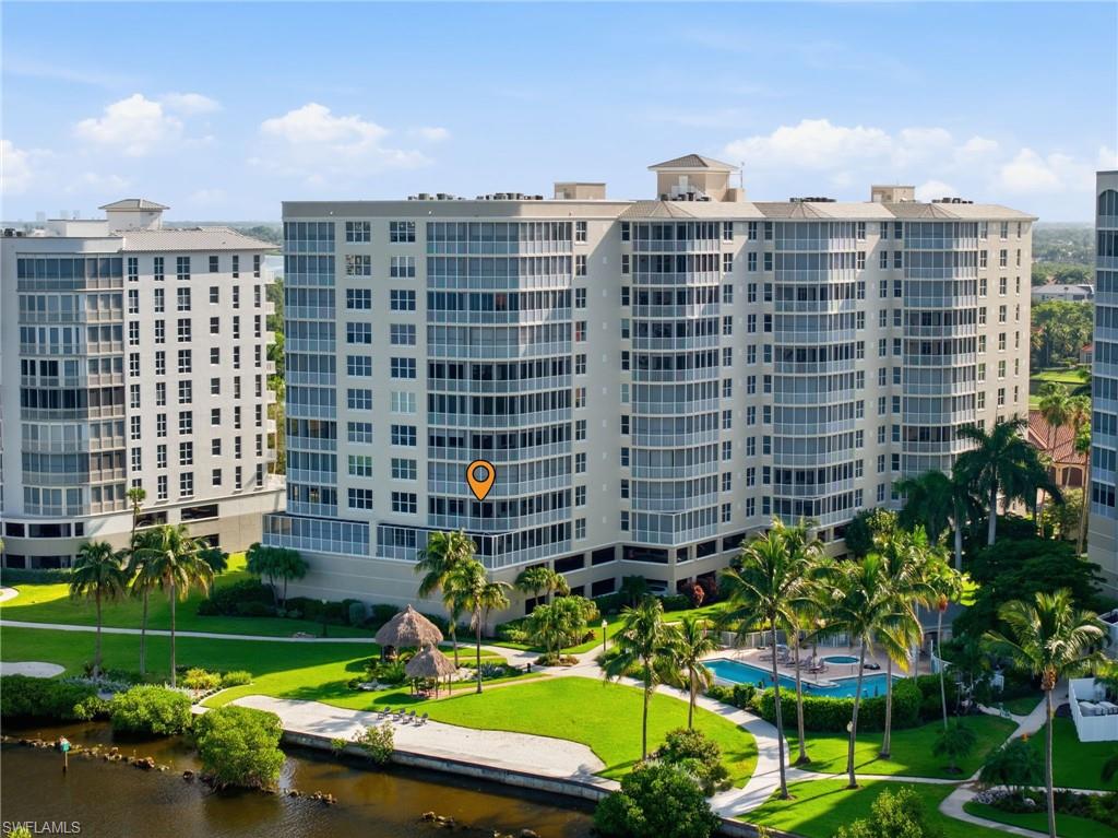 Modern high-rise residential building with multiple balconies, expansive green spaces, a swimming pool, and tropical landscaping