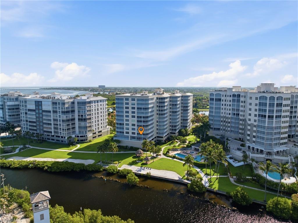 Waterfront condominium building featuring multiple swimming pools, manicured green spaces, and mature palm trees