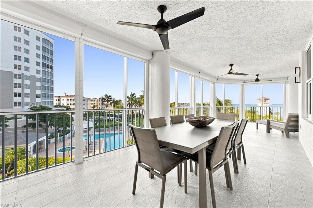 Spacious outdoor living area with a white tiled floor, panoramic window walls, and black ceiling fans