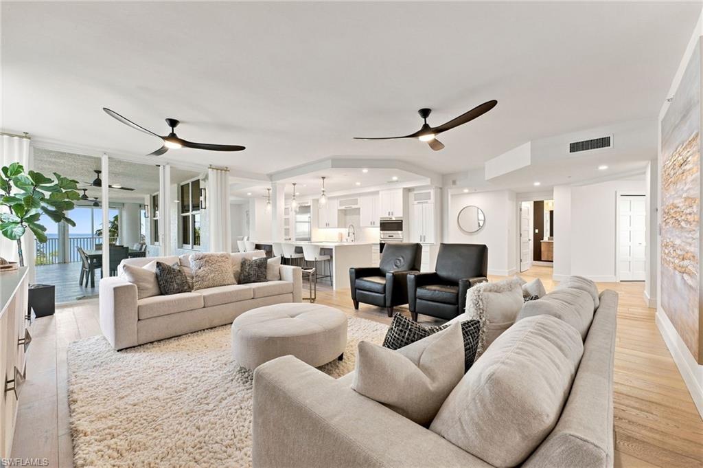 Open-concept living space with light-tone wood flooring, recessed lighting, and a white kitchen featuring a breakfast bar