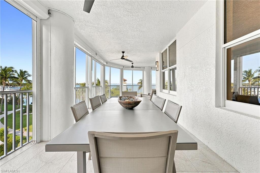 Curved balcony with full-height glass panels, textured ceiling, ceiling fans, wall-mounted light fixtures, and tile flooring