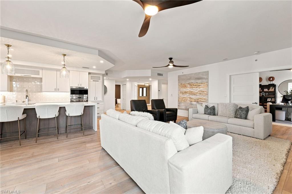 Open-concept living area with wood-finish flooring, white cabinetry, a kitchen island with seating, and recessed lighting