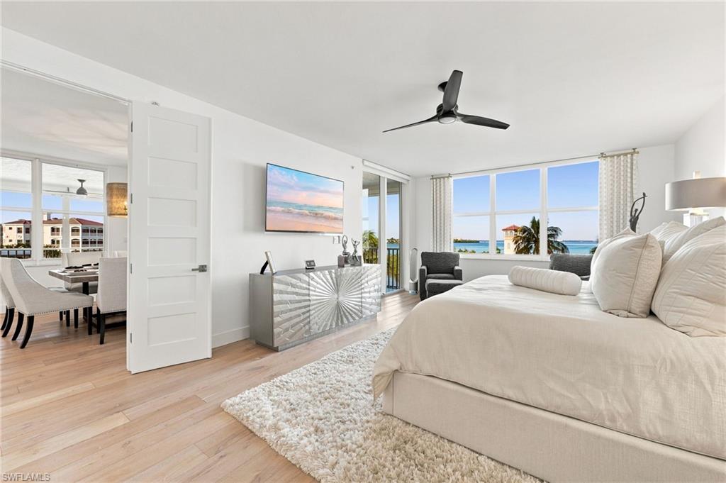 Expansive room with wood-finish flooring, a contemporary ceiling fan, and large windows offering water scenery