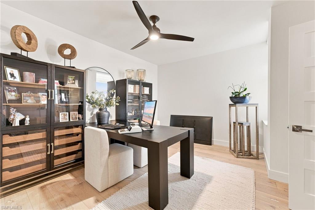 Light wood-finish flooring, built-in shelving with glass-front cabinetry, modern ceiling fan, and white paneled door