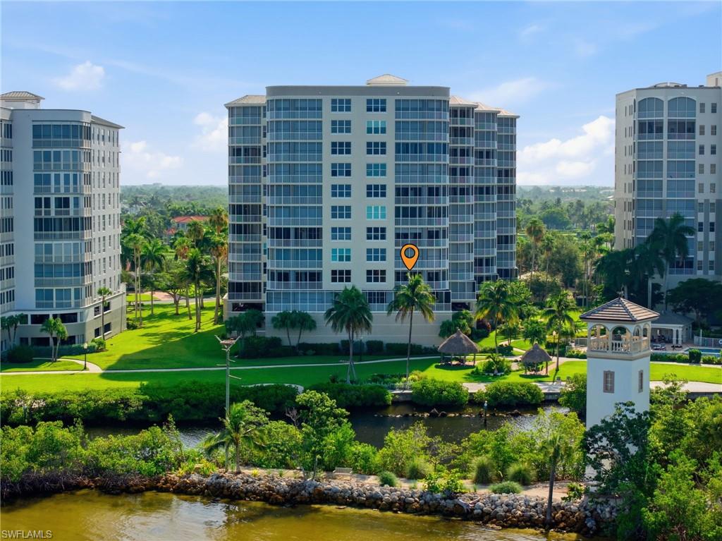 Waterfront high-rise building with a private balcony, surrounded by lush landscaping, a water feature, and a distinctive tower structure