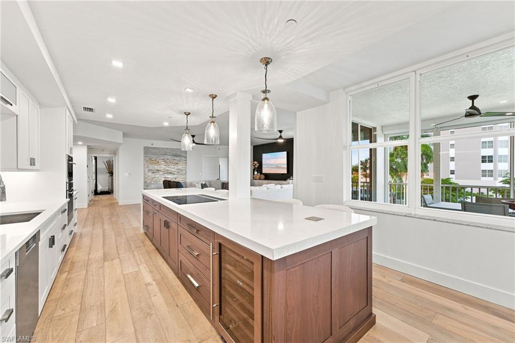 Kitchen featuring a large island with built-in wine refrigeration, white countertops, integrated cooktop, and wood-finish flooring
