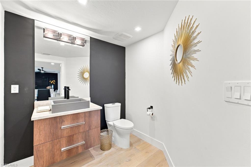 Floating wood-finish vanity with a vessel sink and matte black faucet, illuminated by a three-light fixture