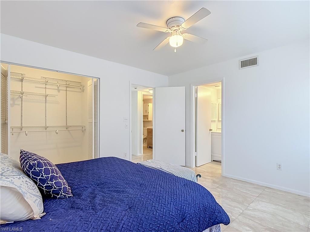 Spacious bedroom featuring light-toned tile flooring, a ceiling fan with integrated lighting, and a built-in closet with wire shelving