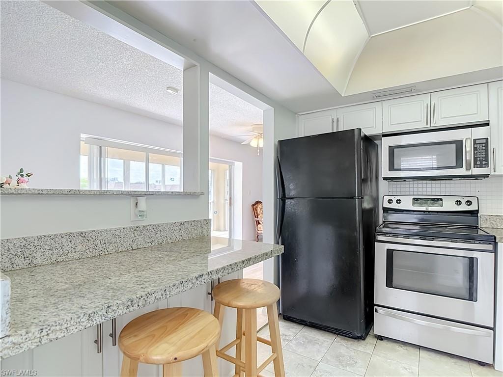 Kitchen featuring white shaker-style cabinetry, granite-finish countertops, stainless steel electric range, and an over-the-range microwave