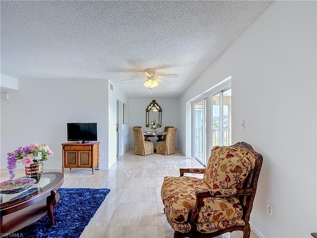Open living area featuring light-toned tile flooring, white wall finishes, and a textured ceiling