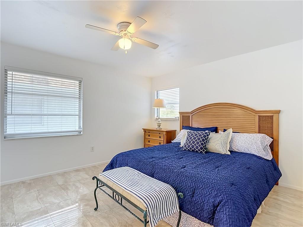 Spacious room featuring a wood-finish headboard, light-toned tile flooring, and a ceiling fan with integrated lighting