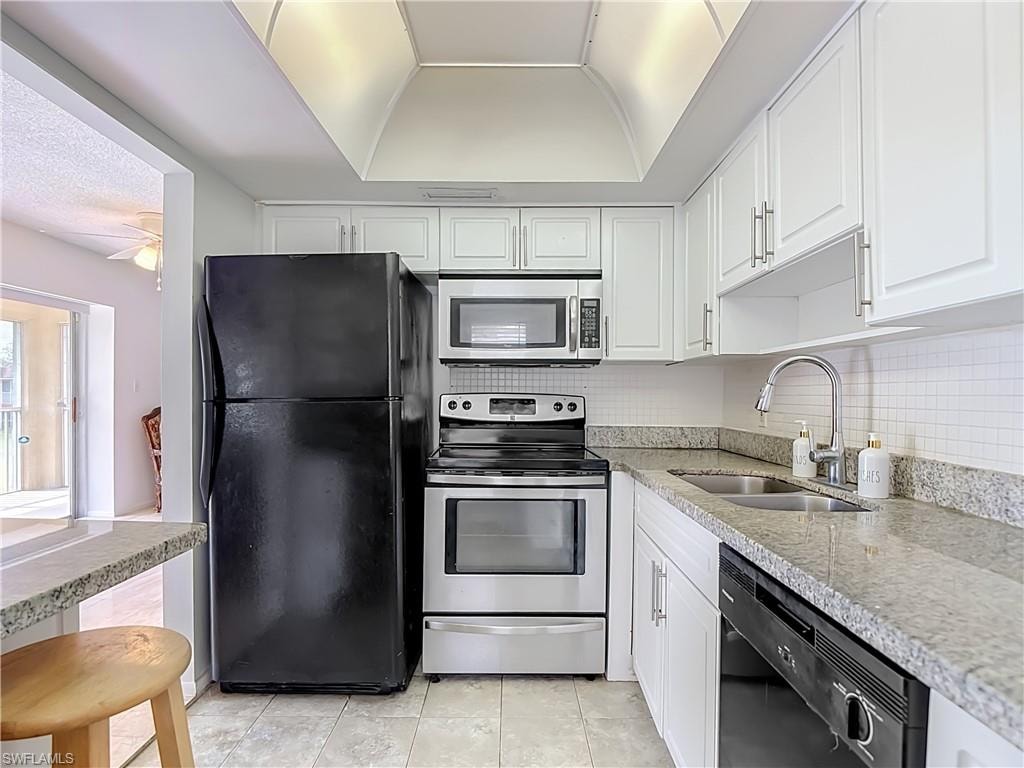 Kitchen featuring white cabinetry, light-toned countertops, a full suite of appliances, a double basin sink, and tile flooring