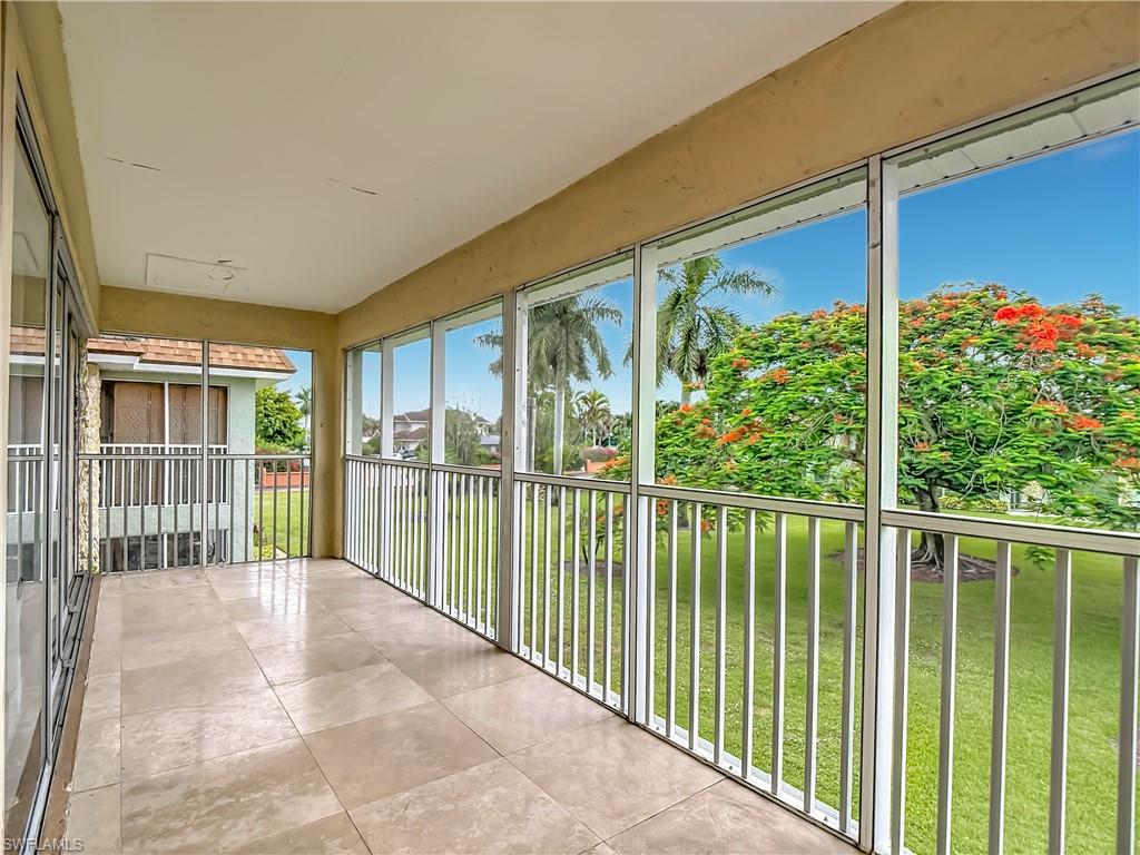 Screened balcony featuring light-toned tile flooring, white vertical railings, and expansive views of lush landscaping with mature palm and flowering trees